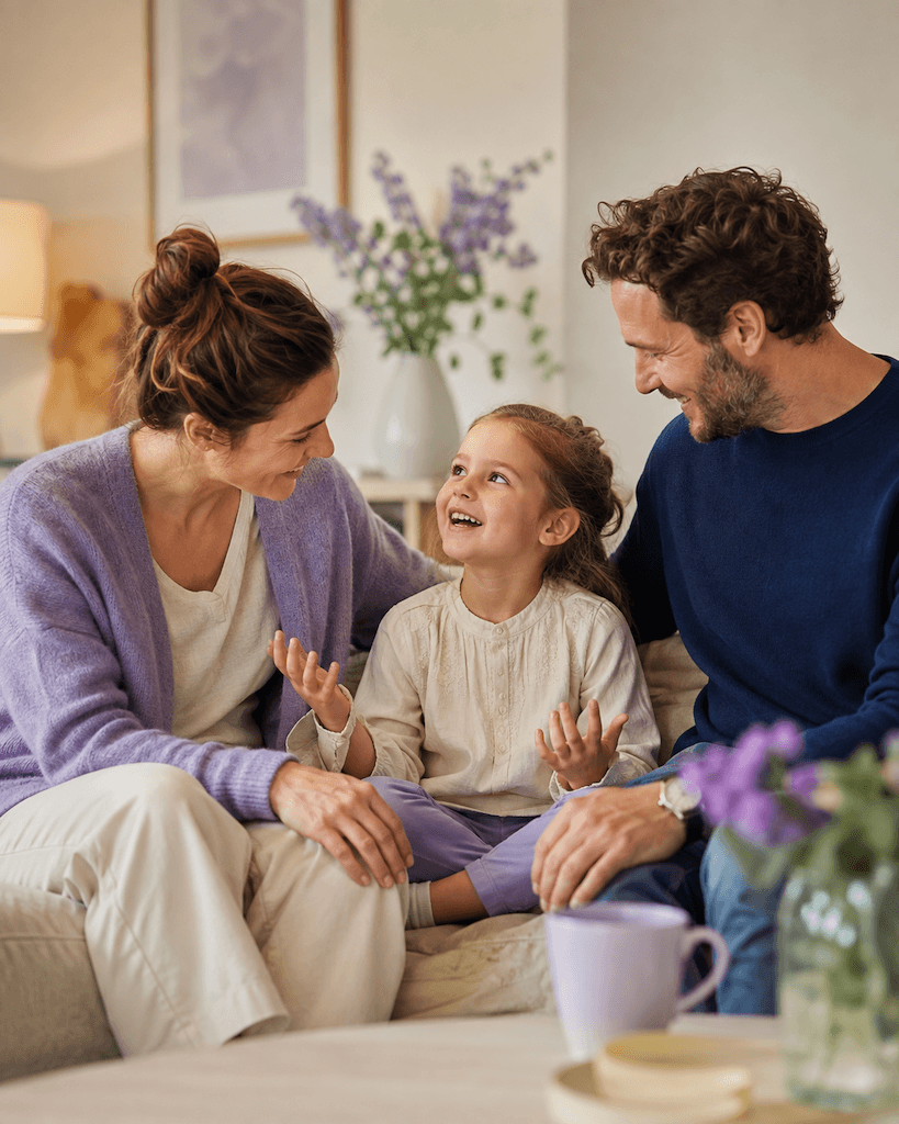 Kind spricht zu Hause entspannt und fröhlich mit einem Elternteil in vertrauter Umgebung (KI-generiert)