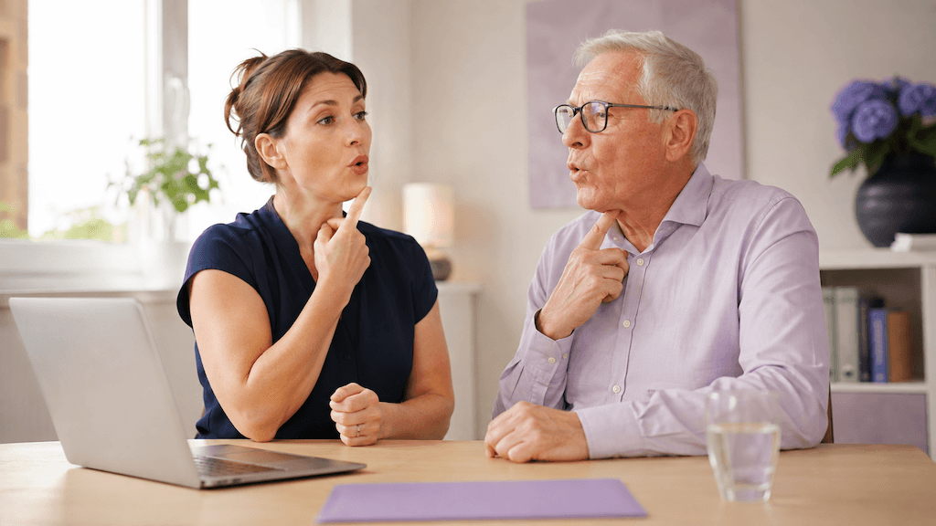 Logopädin übt auf Augenhöhe mit einem älteren Menschen Stimme und Aussprache in der Dysarthrietherapie (KI-generiert)