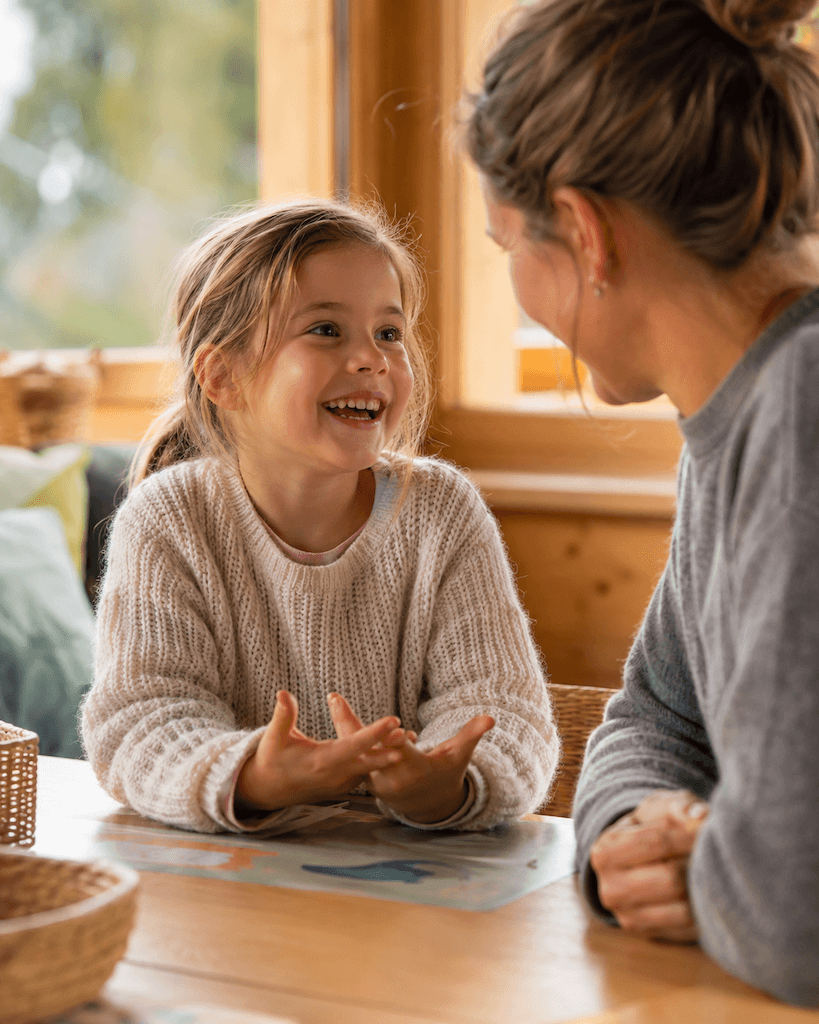 Vorschulkind spricht unbeschwert und lachend mit einem zugewandten Erwachsenen (KI-generiert)