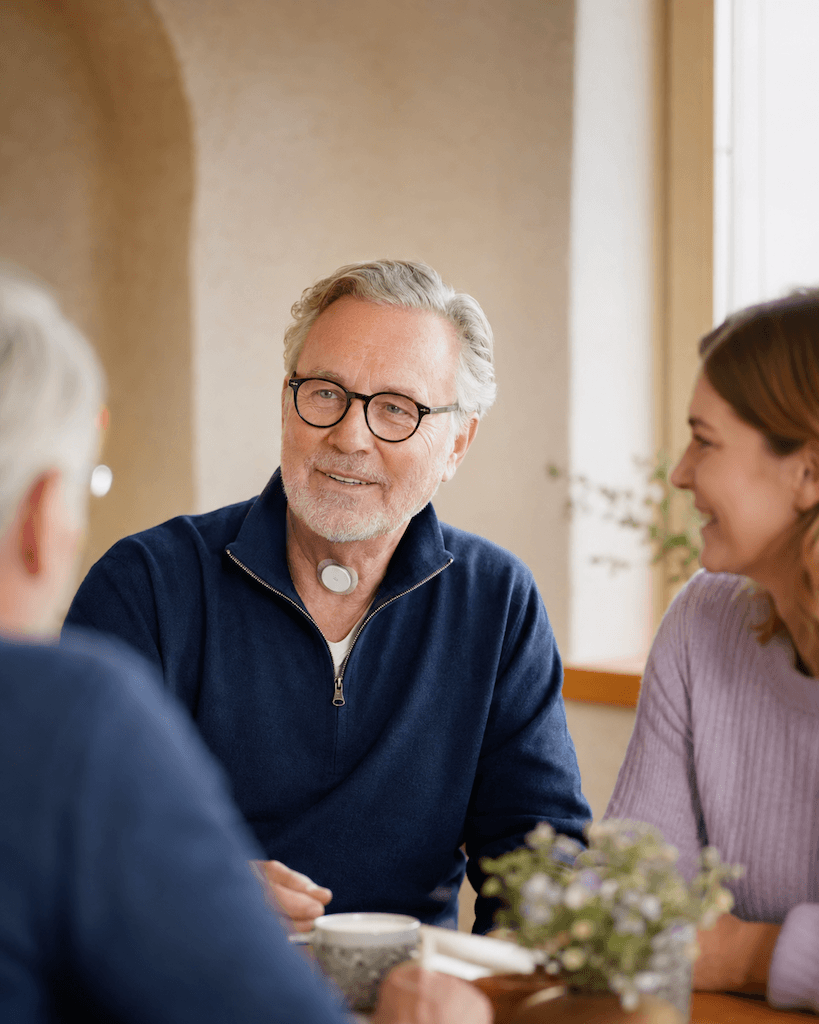 Älterer Mensch nach einer Kehlkopfentfernung in einer positiven, würdevollen Gesprächssituation mit Angehörigen (KI-generiert)